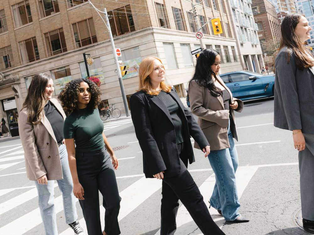 Five women from a Toronto PR and marketing agency walking together across a downtown crosswalk during a city photo shoot.