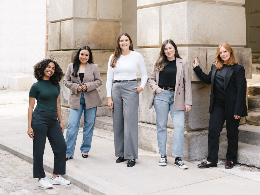 Five women from a Toronto PR and marketing agency standing outside a historic stone building in business-casual attire.